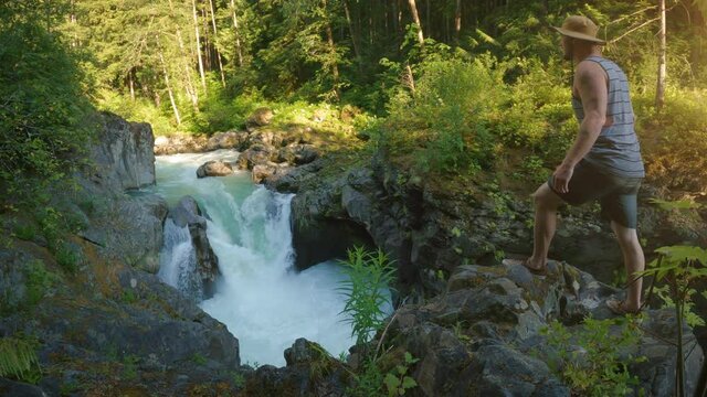 Man on Wilderness Adventure Stops to View Raging Waterfall in Rocky Canyon