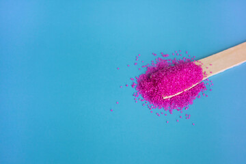 Cosmetic pink salt scattered on a wooden spatula on a blue background.Salt for bath, spa treatments.