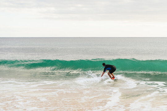 Caucasian hispanic man surfing on a skimboard next to a wave at sunset on the beach