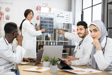 Fototapeta premium Multiethnic medical workers gathering at conference room for daily briefing. Men and women in uniform working on modern gadgets. Concept of people, technology and medicine.
