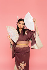 Asian woman in kimono holding fans isolated on pink
