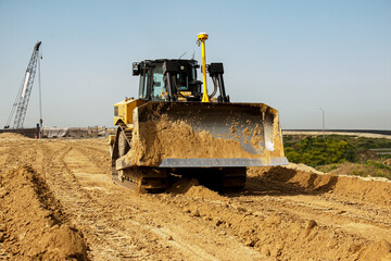 Asphalt road construction process. The bulldozer levels and compacts the clay soil for the base of the highway. Earthworks on a summer day.