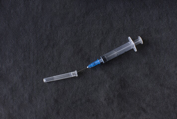 a disassembled medical syringe for injection with a metal needle lies on a dark gray fabric background