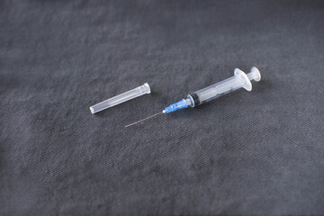 a disassembled medical syringe for injection with a metal needle lies on a dark gray fabric background