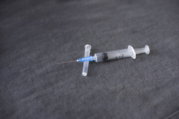 a disassembled medical syringe for injection with a metal needle lies on a dark gray fabric background