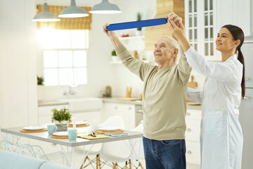 Fototapeta premium Thoughtful young nurse helping an elderly man to do exercises at home