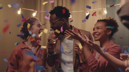 Waist-up slowmo of young happy friends celebrating party with champagne and confetti having fun together