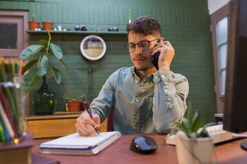 young adult sitting at his desk, making a phone call