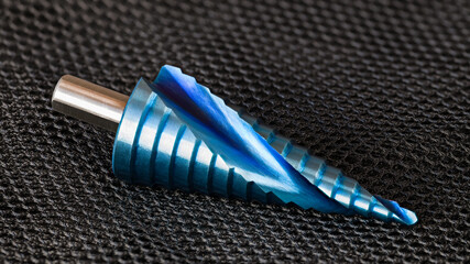 Closeup of conical step drill bit with spiral flute and blue surface finish on grid net black...