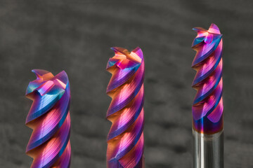 Three steel end mills with beautiful colored nano coating on gray background. Closeup of sharp...