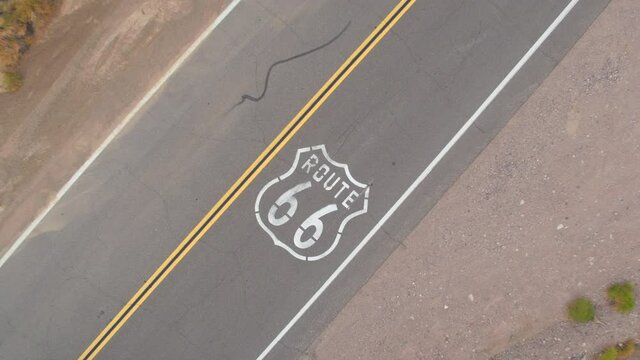 TOP DOWN: Scenic aerial shot of a tourist car driving down the famous Route 66 in rural California. Drone point of view of an empty asphalt interstate freeway crossing the rugged American terrain.