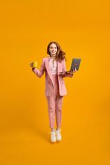 Full length profile photo of funny business lady jump high up hold laptop and cup of coffee in hands addicted worker always online wear pink suit outfit, white sneakers, isolated yellow background