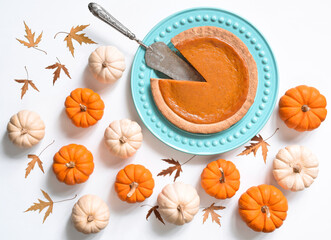 Overhead view of pumpkin pie surrounded by mini pumpkins on white background