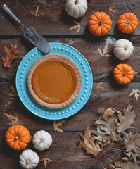 Overhead view of pumpkin pie surrounded by mini pumpkins on rustic wooden table