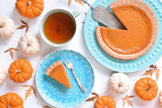 Overhead View Of Pumpkin Pie And Cup Of Tea Surrounded By Mini Pumpkins On White Background