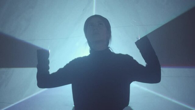 Silhouette of young woman standing in laser tunnel in dark studio and moving her hands through projection