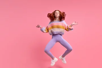 Fototapeten Lotusblume pretty redhead lady jumping high sitting air in lotus pose practicing morning yoga wearing casual outfit isolated pastel pink color background, portrait. Calm caucasian female meditating  © alfa27