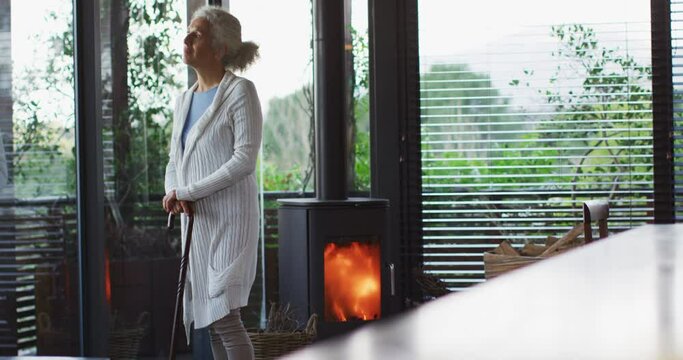 Senior mixed race woman leaning on walking cane standing next to fireplace