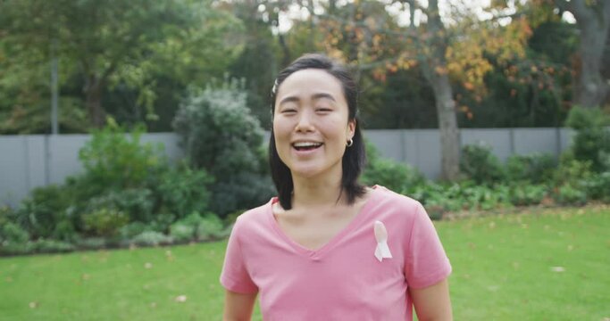 Portrait of happy asian woman wearing pink t shirt and cancer ribbon, standing in garden laughing