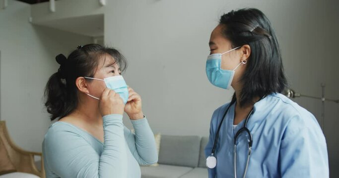 Asian female nurse and patient wearing face masks talking and looking to camera in hospital