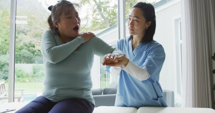 Asian female physiotherapist treating female patient at surgery, moving her arm