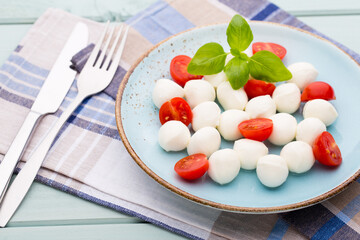 Delicious caprese salad with ripe cherry tomatoes and mini mozzarella cheese balls with fresh basil leaves.