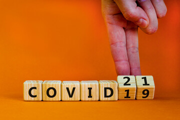 Symbol of covid-19 pandemic in 2021 year. Businessman turns wooden cubes and changes words 'covid-19' to 'covid-21'. Beautiful orange background, copy space. Medical, 2021 year covid-21 concept.
