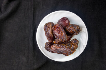 Big luxury dried date fruit in bowls on the dark surface, kurma ramadan kareem concept, close up.
