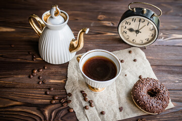 glass of coffee on table with clock in morning. vintage alarm clock showing 9am on the table next to a cup of coffee and a doughnut. Breakfast. Time management concept