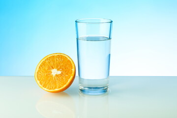 a glass of water and half of orange on blue background with copy space. vitamin C concept. 