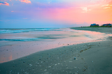 A long exposure of waves on the pink sand at Holly Beach, Louisiana, at sunset.