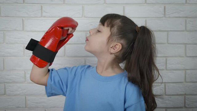 Little girl in kickboxing gloves. Cute little girl blowing on her nails with kidboxing gloves.