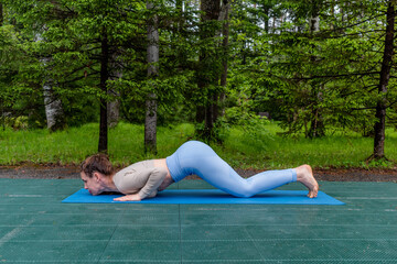 Candid red-haired woman doing yoga outdoors in the park. Sportswear and yoga mat. Copy space