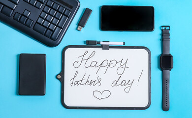 Keyboard, smartphone and whiteboard.
Keyboard, smartphone, wrist watch, hard drive and white board with the inscription: Happy Father's Day lie on a blue background, close-up top view.