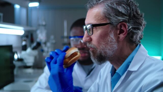 Man tasting burger with lab grown meat near colleague