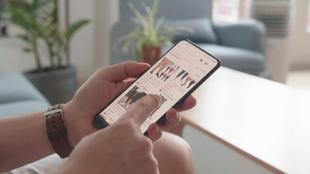 Close Up Of Man Hand Holding Smartphone And Doing Online Shopping At Home, Male Looks At Goods In Online Store Clothing
