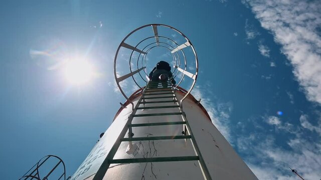 Male worker up the ladder is for inspection shell plate top of storage tank chemical.