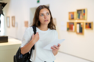 Portrait of a young girl visitor with a paper guide at the exhibition of paintings in the museum..