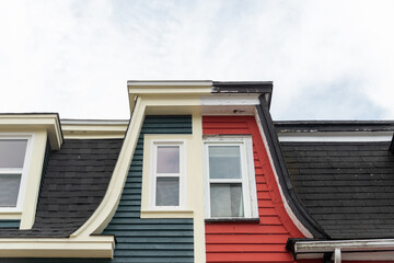 Two vintage wooden adjoined houses, one green one red, with multiple double hung windows, clapboard, and a hip roof. The houses have a flat roof with a hip roof on the front covered in black shingles.