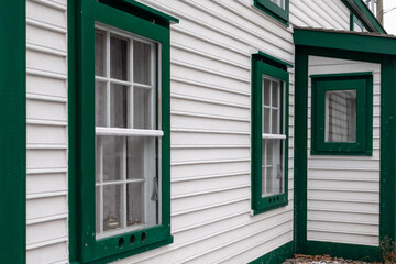 Fototapeta premium A vintage style one and a half story building. The vernacular structure is clad in cape cod clapboard with multi-panes and a number of single hung windows. The white building has green trim.