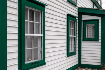 A vintage style one and a half story building. The vernacular structure is clad in cape cod clapboard with multi-panes and a number of single hung windows. The white building has green trim.