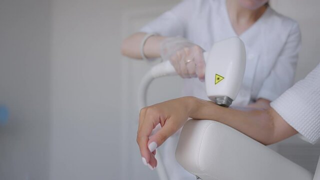 Procedure of removing hairs on hand. Laser hair removal on a diode laser, tracking moving camera. Woman cosmetologist applies laser hair removal gel on female hand. photoepilation, body care concept.