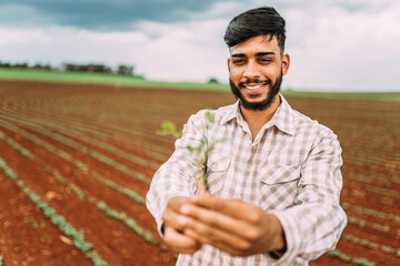 Latin young farmer man hands holding a green young plant. Symbol of spring and ecology concept.