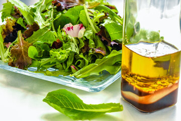 green salad on a glass plate with bottle of salad dressing behind it on a white table