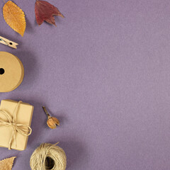 Fototapeta na wymiar Brown gift box, string, wooden clip, dry flowers on purple background. flat lay, top view, copy space