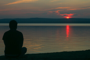the silhouette of a man on the sand who looks at the sunset sun