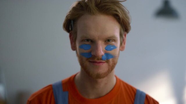 Cheerful Man Putting War Paint On Face During House Renovation In New Home.