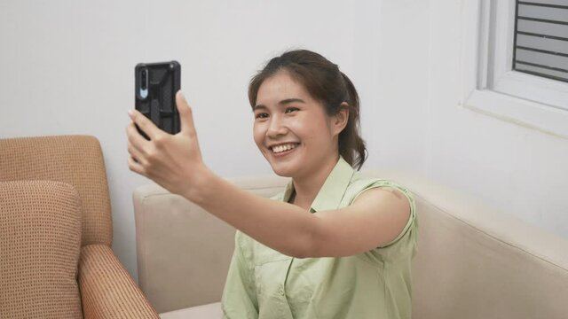 Asian young woman use smartphone video call to friend she pointing to adhesive plaster on arm her vaccinated certificate after getting vaccine prevent at home