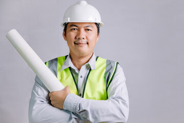 A young architect or engineer wearing a reflective vest and safety helmet in construction work, a young professional architect holding a blueprint for his design work.