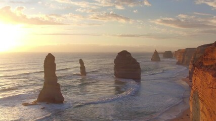 AERIAL: Golden sunshine illuminates the cliffs and other rock formations on coast of Australia. Spectacular drone point of view of the famous 12 Apostles beach in Australia on a sunny summer evening.